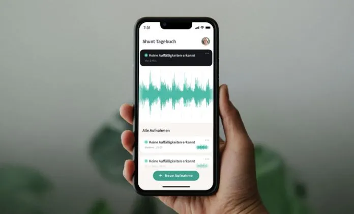 Hand, die ein Smartphone hält, auf dem eine App geöffnet ist. In der App ist ein Diagramm zu sehen und verschiedene Einträge eines "Shunt Tagebuchs".